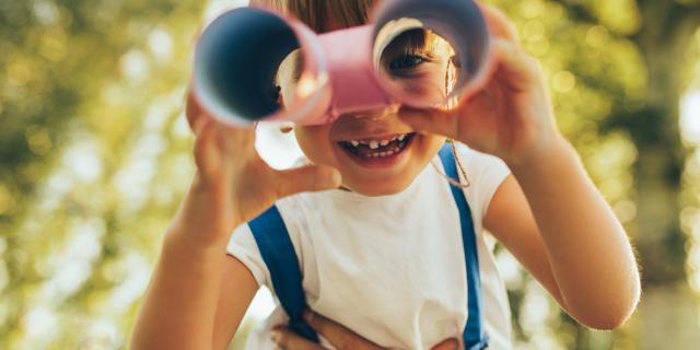 Closeup image of cute little boy playing with a binoculars searching for an imagination or exploration in summer day in park. Happy child playing pretend safari game outdoors in the forest. Childhood