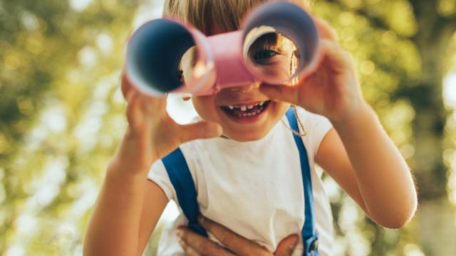 Closeup image of cute little boy playing with a binoculars searching for an imagination or exploration in summer day in park. Happy child playing pretend safari game outdoors in the forest. Childhood