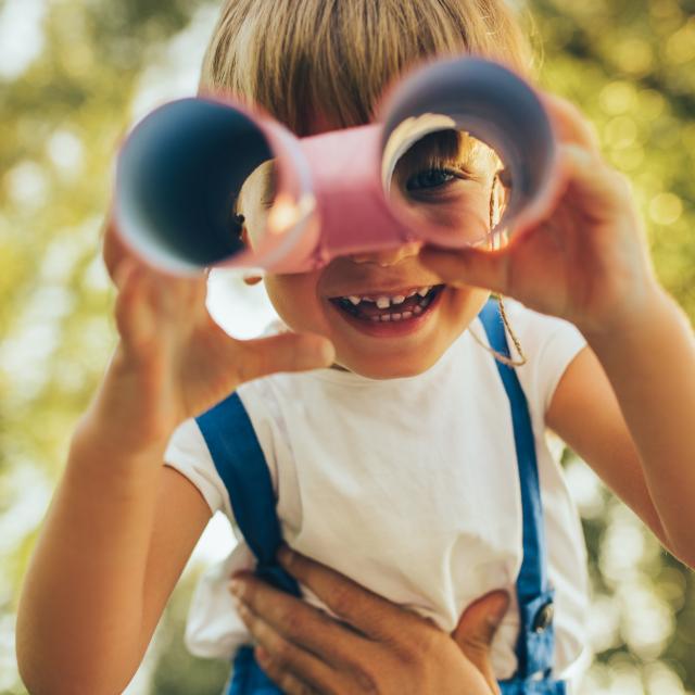 Closeup image of cute little boy playing with a binoculars searching for an imagination or exploration in summer day in park. Happy child playing pretend safari game outdoors in the forest. Childhood