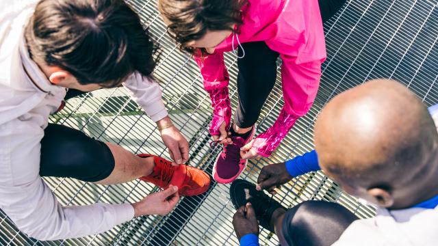 Multiethnic group of runners getting ready for a workout session - Athletes tying shoelaces and resting after a run outdoors