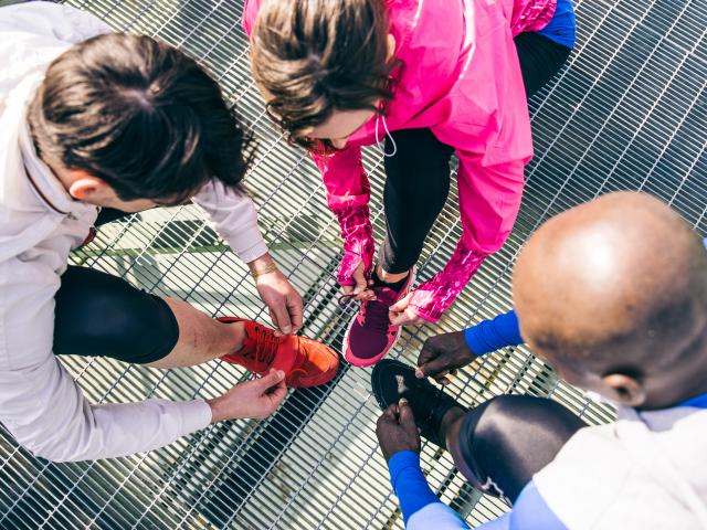 Multiethnic group of runners getting ready for a workout session - Athletes tying shoelaces and resting after a run outdoors