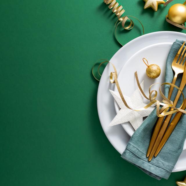 Christmas Flat Lay Background. Gold Cutlery with Bubbles served on napkin on plate on Green Background. Minimalistic design. Copy Space. Horizontal. Christmas concept. 