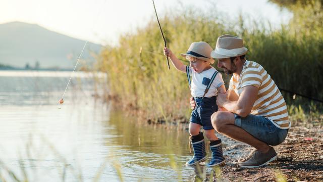 A mature father with a small toddler son outdoors fishing by a river or a lake.