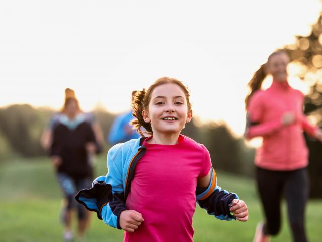 A portrait of small girl with large group of people running in nature.