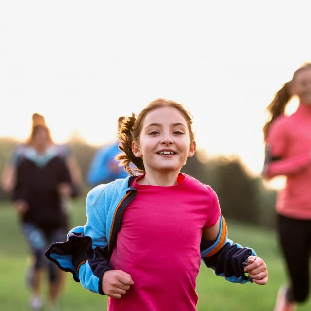 A portrait of small girl with large group of people running in nature.