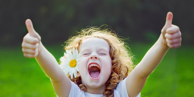 Laughing girl with daisy in her hairs, showing thumbs up.