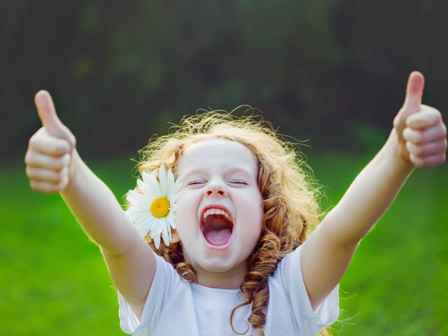 Laughing girl with daisy in her hairs, showing thumbs up.