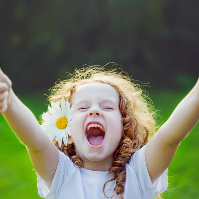 Laughing girl with daisy in her hairs, showing thumbs up.